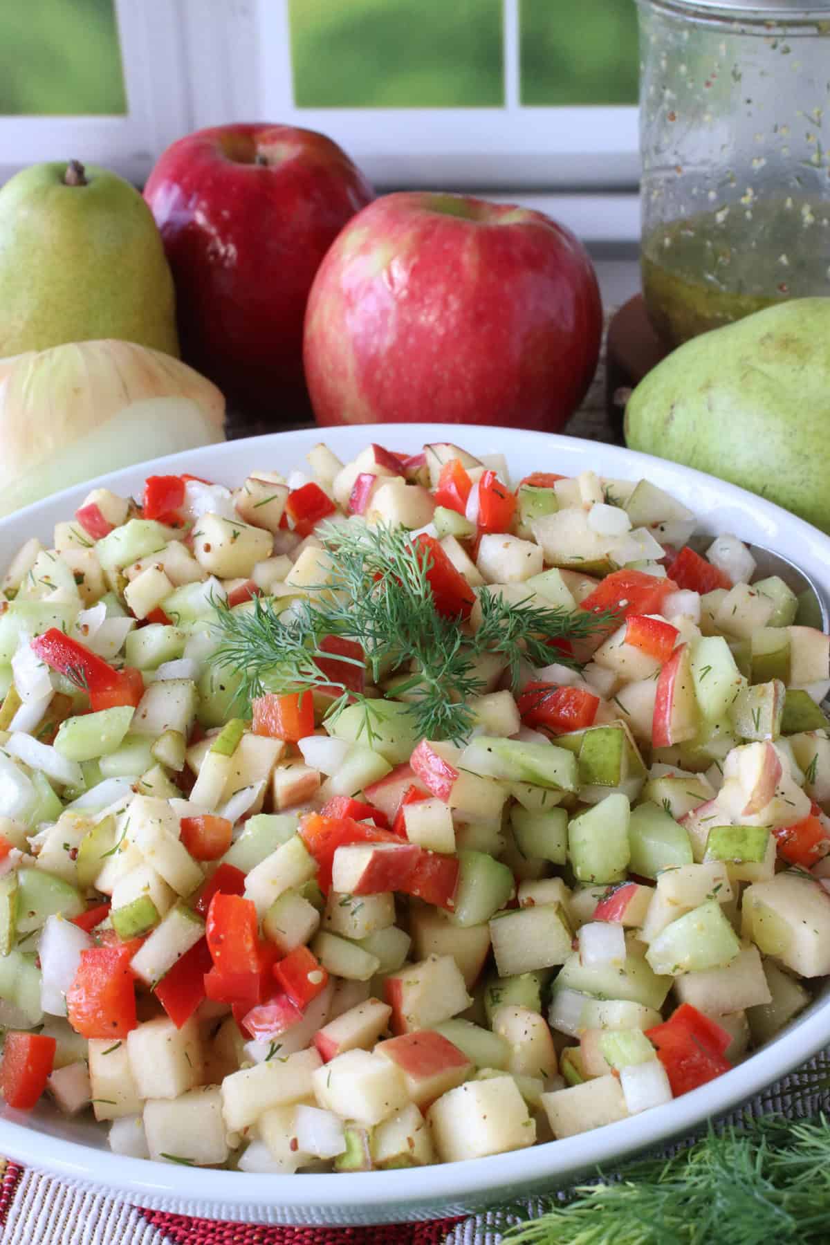 Fresh apples, pears, and onions behind a bowl of chopped fruit and vegetable salad.