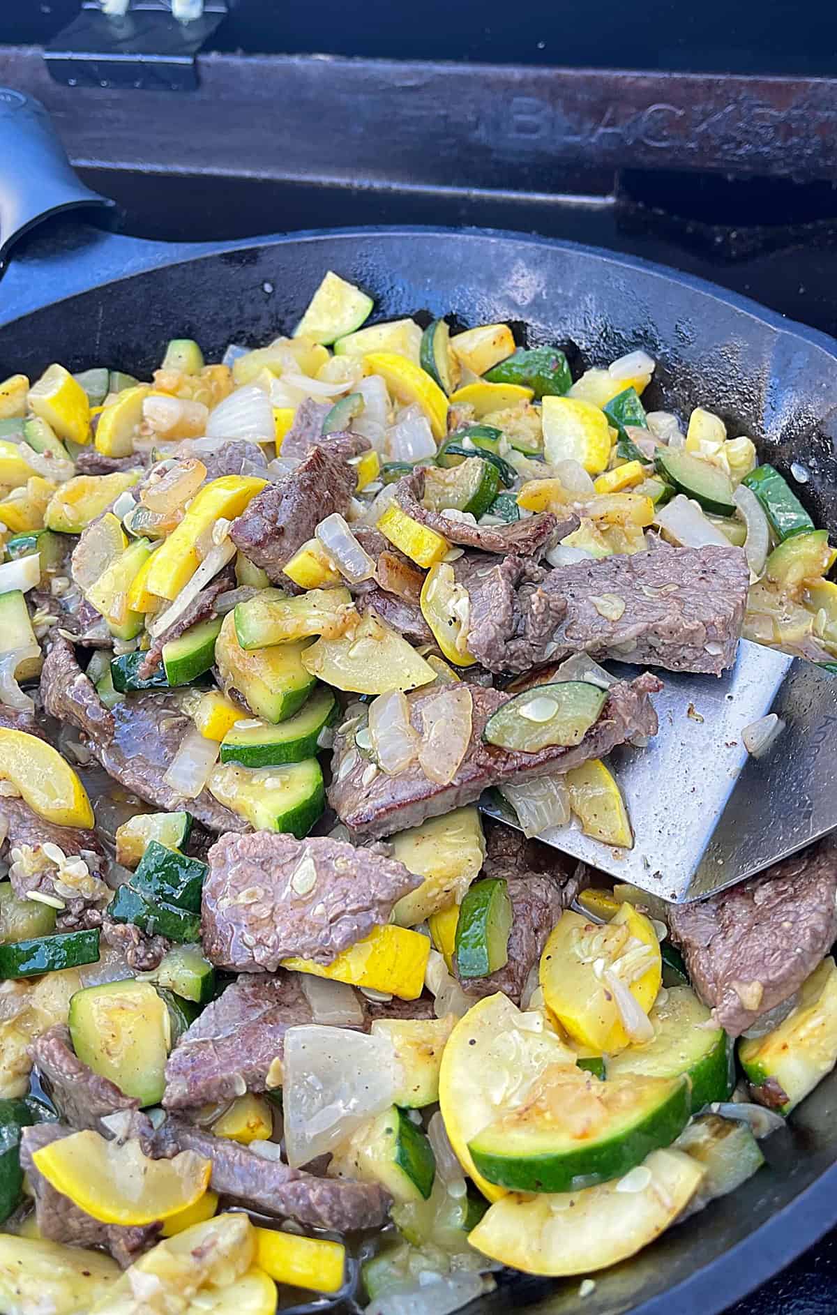 Cooked flank steak, zucchini, and summer squash in a cast iron skillet.