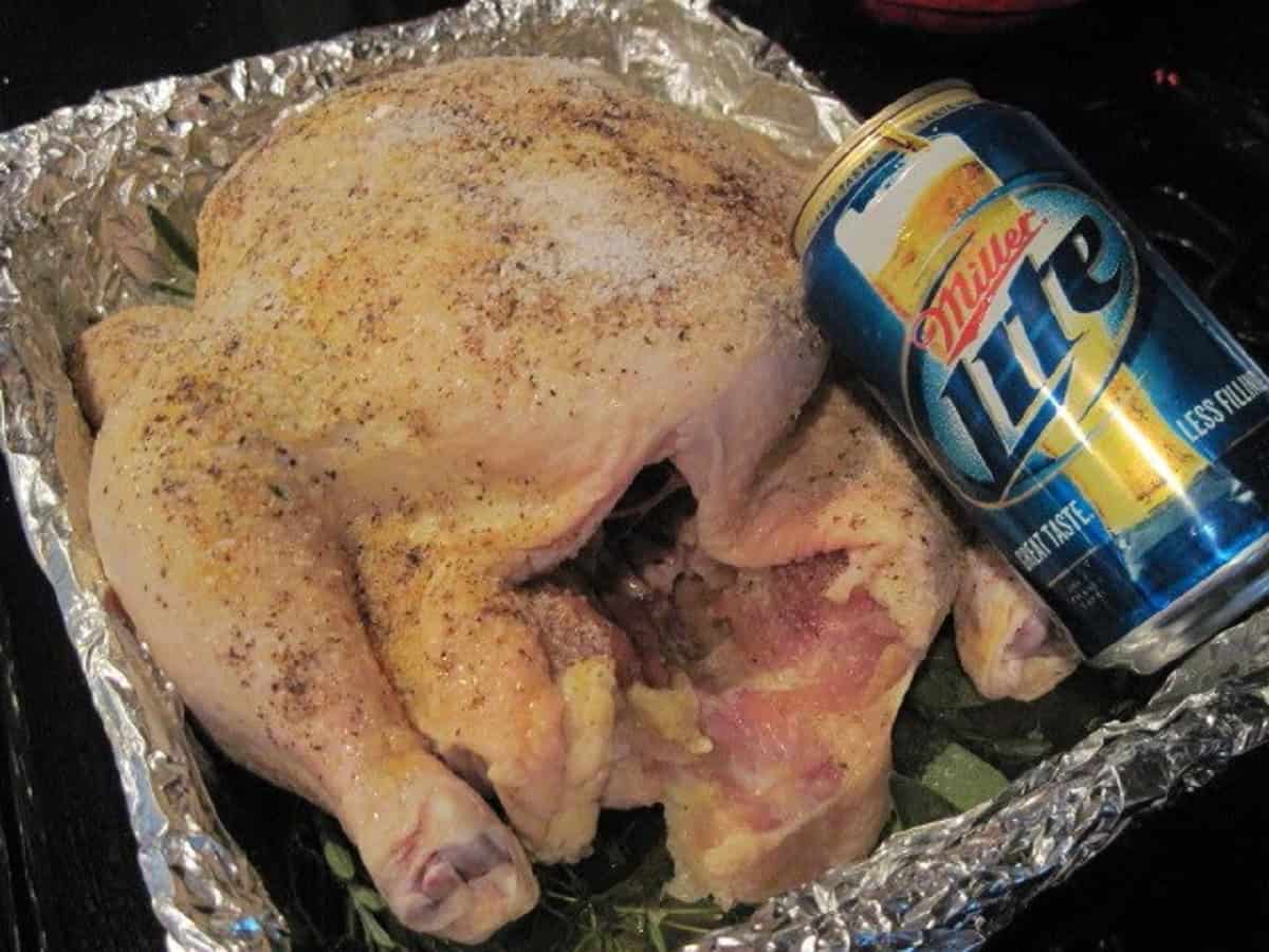 A can of beer next to a chicken in a roasting pan.