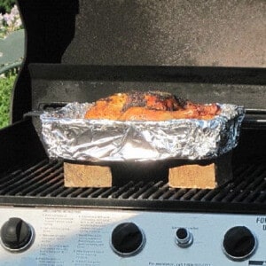 A pan covered with foil on the grill with a Grilled Beer Chicken inside.