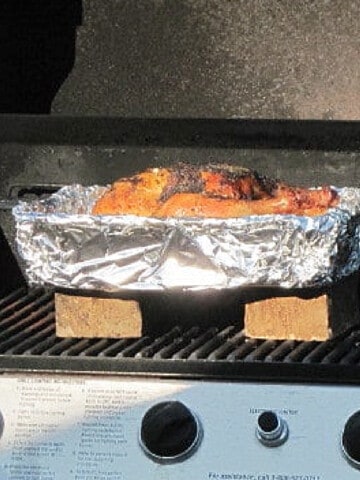 A pan covered with foil on the grill with a Grilled Beer Chicken inside.
