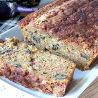 A loaf of sliced eggplant zucchini bread on a white rectangular plate with a eggplant and zucchini in the background.