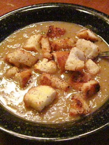 A black bowl filled with a serving of French Onion Lentil Soup with homemade croutons on top.