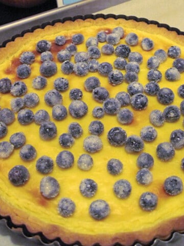 A Crostata with Pastry Cream topped with sugared blueberries in a tart pan on a baking sheet.