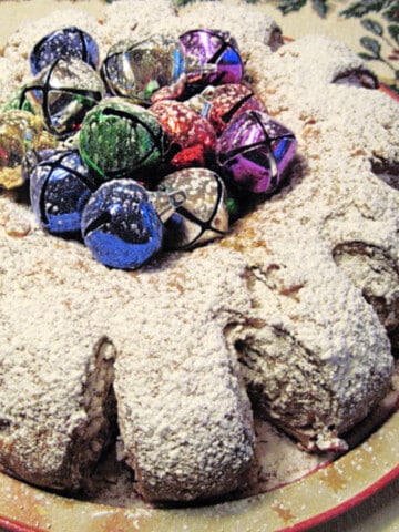 A traditional German Stollen decorated with multi colored bells and powdered sugar on top.