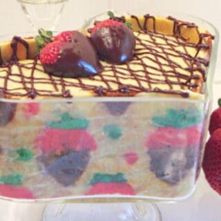A glass heart trifle dish filled with a Chocolate Covered Strawberry Joconde Entremet with fresh strawberries on the side.