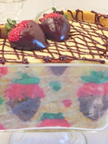 A glass heart trifle dish filled with a Chocolate Covered Strawberry Joconde Entremet with fresh strawberries on the side.