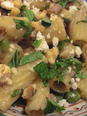 An overhead closeup photo of a serving of Greek Pasta with Lamb and chopped mint along with feta cheese and walnuts.