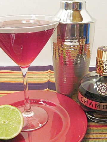 A Cham Wow Cocktail in a martini glass along with a cocktail shaker in the background.