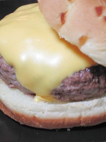 A super closeup of a Ground Beef Burger on a bun with a slice of melted American cheese.