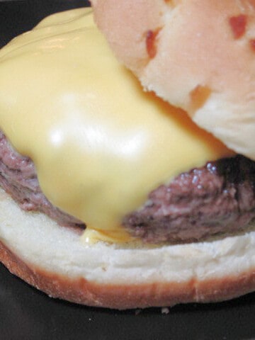 A super closeup of a Ground Beef Burger on a bun with a slice of melted American cheese.