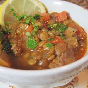 A small white bowl filled with Lentil Stew with Lemon and Sausage along with carrots.