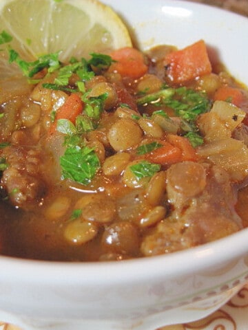 A small white bowl filled with Lentil Stew with Lemon and Sausage along with carrots.