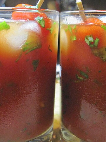 A closeup of two Italian Caprese Cocktails in glasses with ice and chopped basil.