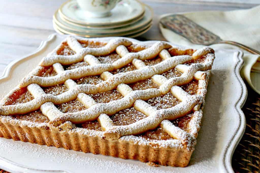 A horizontal photo of Old-Fashioned Apple Sauce Cake on a pretty square plate with china cup and saucer in the background.