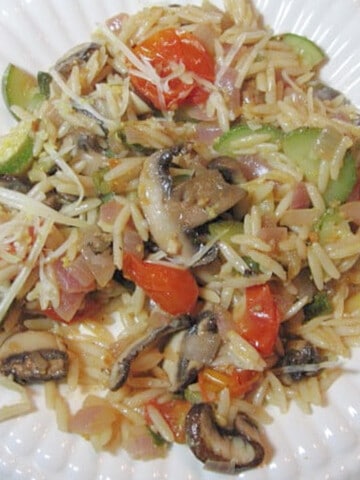 A white plate filled with a serving of Orzo Vegetable Pasta with mushrooms, red peppers, and zucchini.