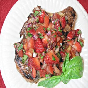 A directly overhead photo of a Pork Chop with Strawberry Relish on a white plate with fresh basil as garnish.