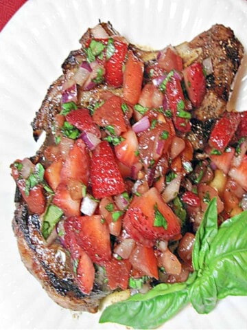 An overhead photo of a Pork Chop with Strawberry Relish on a white plate with fresh basil as garnish.