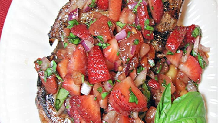 A directly overhead photo of a Pork Chop with Strawberry Relish on a white plate with fresh basil as garnish.