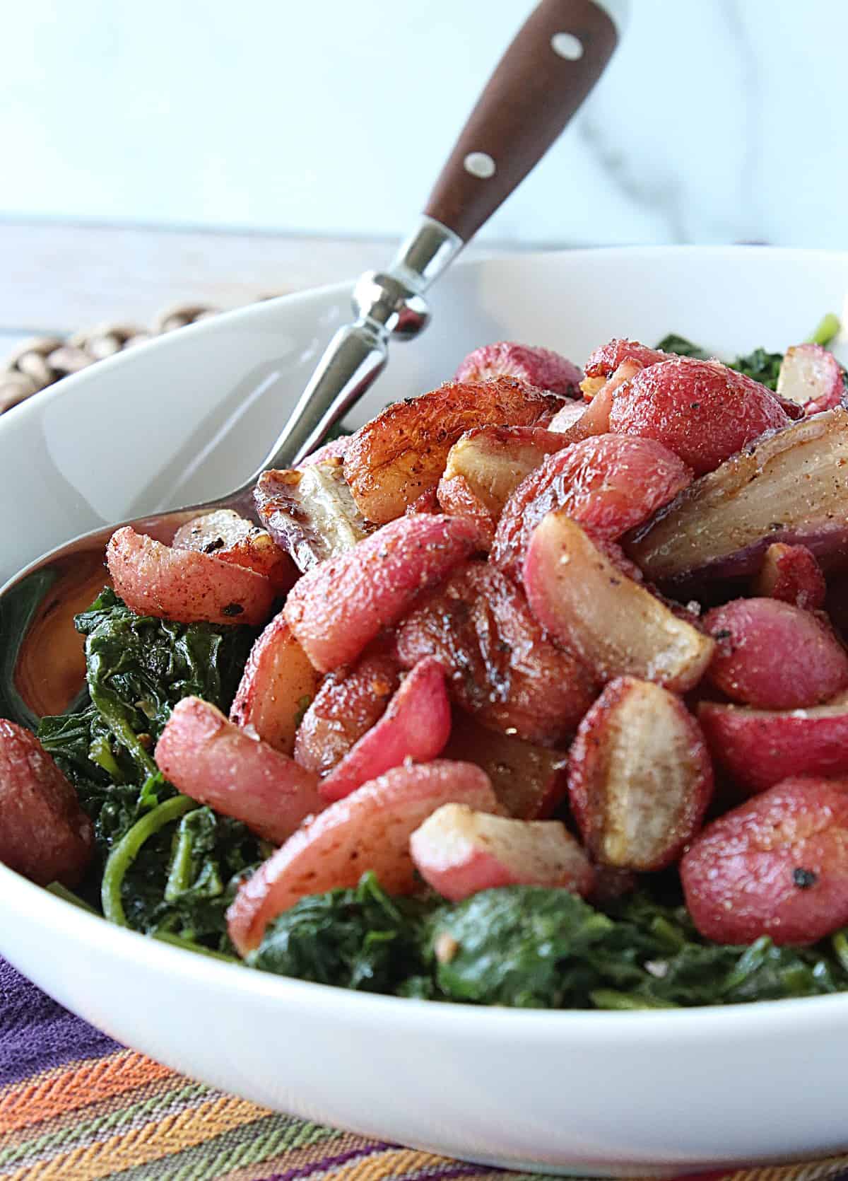 A spoon in a white bowl of Roasted Radishes with sauteed radish greens.