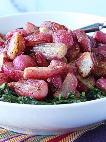 A white bowl filled with Roasted Radishes and greens.