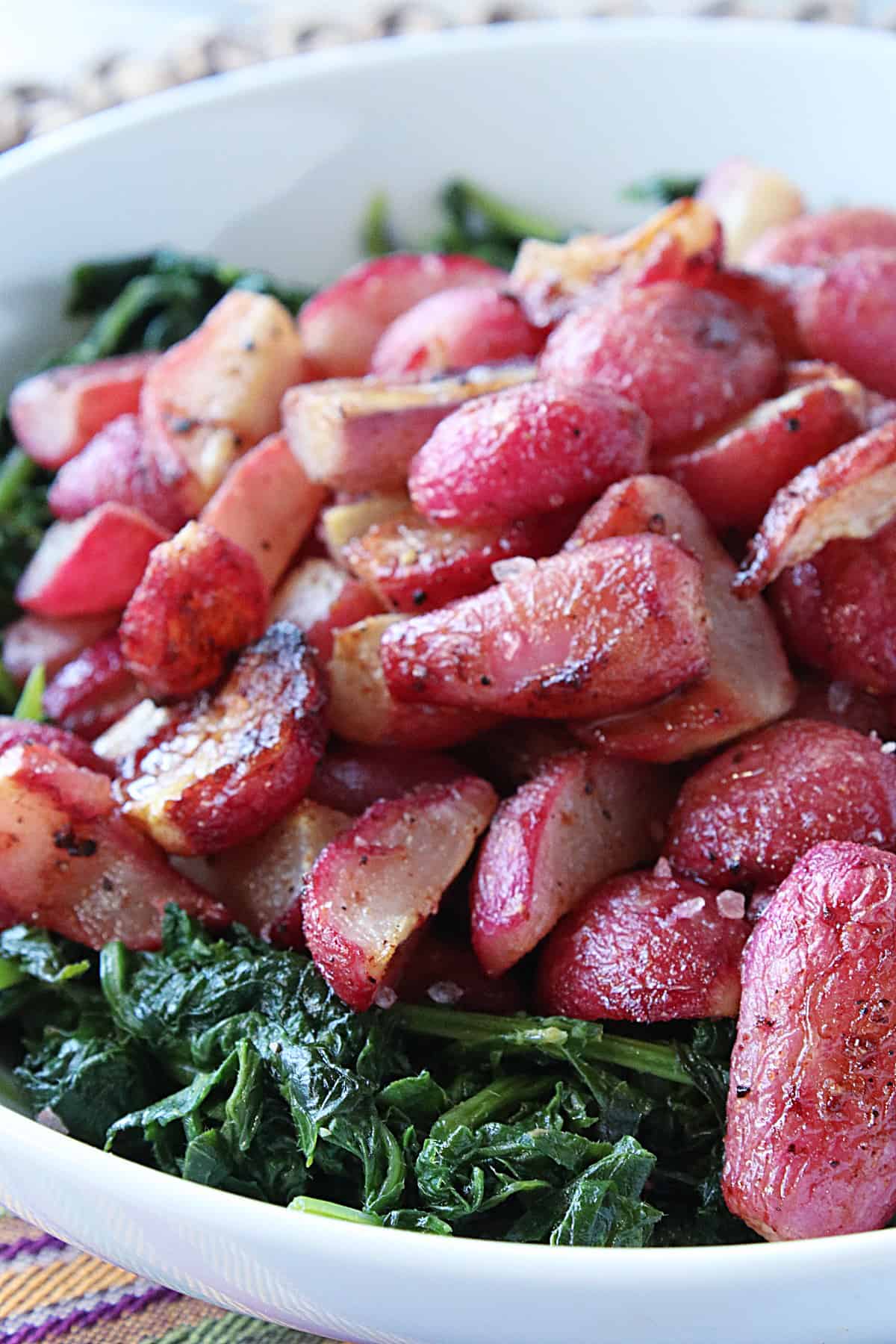 A white bowl with red Roasted Radishes and greens.