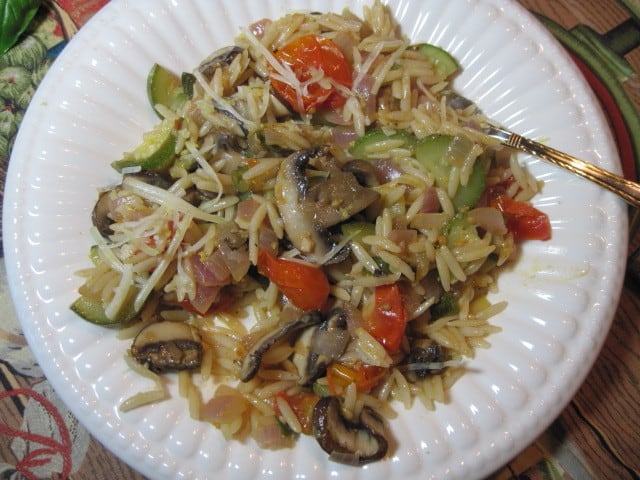 A white plate filled with a serving of Orzo Vegetable Pasta with mushrooms, red peppers, and zucchini.