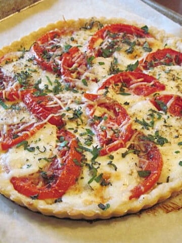 A round Caprese Tomato Tart on a baking sheet topped with basil.