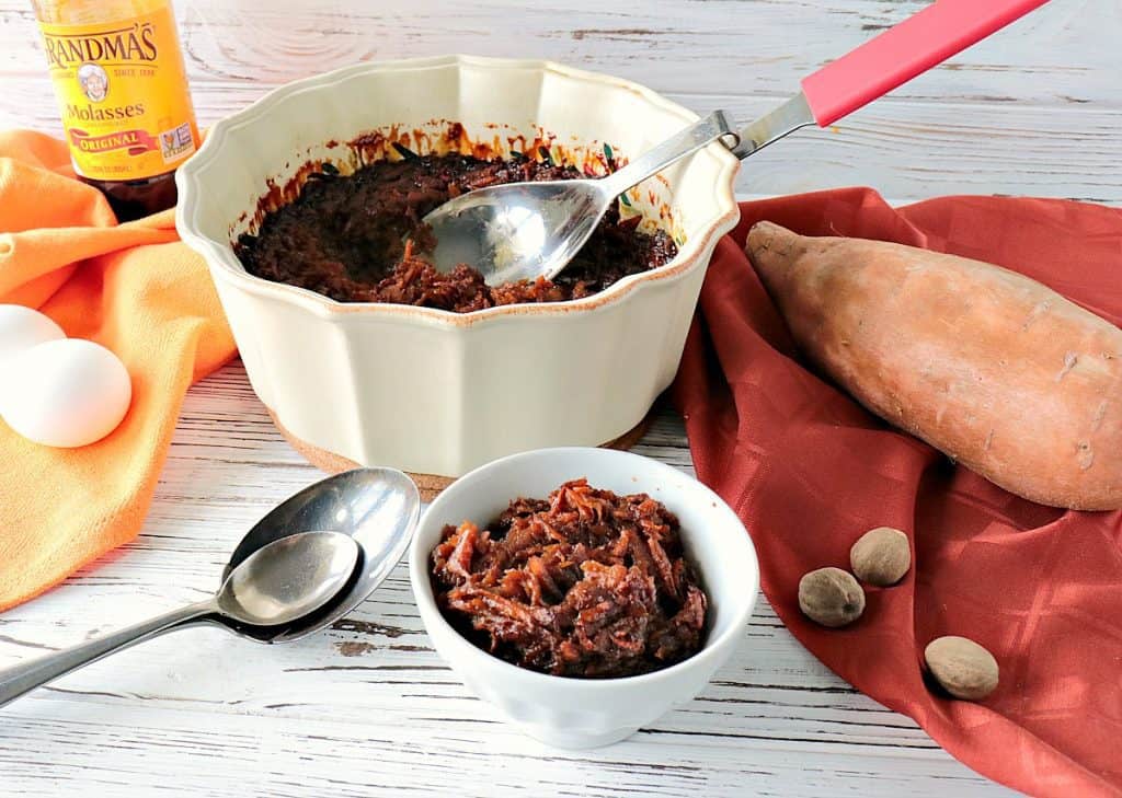 A small bowl of Old-Fashioned Grated Sweet Potato Pudding along with a large bowl in the background with an orange napkin.