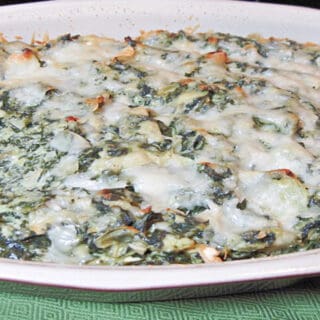 An oval casserole dish filled with Spinach Artichoke Dip topped with cheese.