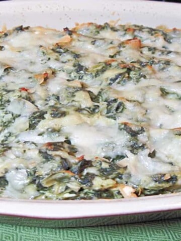 An oval casserole dish filled with Spinach Artichoke Dip topped with cheese.