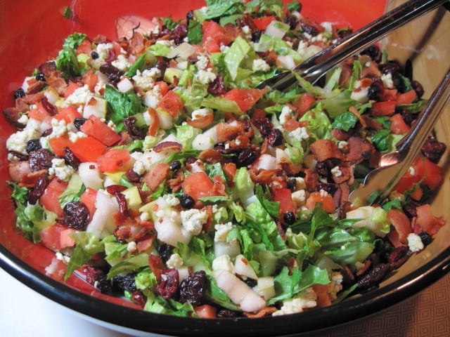 A colorful bowl filled with Winter Chopped Salad with cranberries, bacon, lettuce, and pecans.