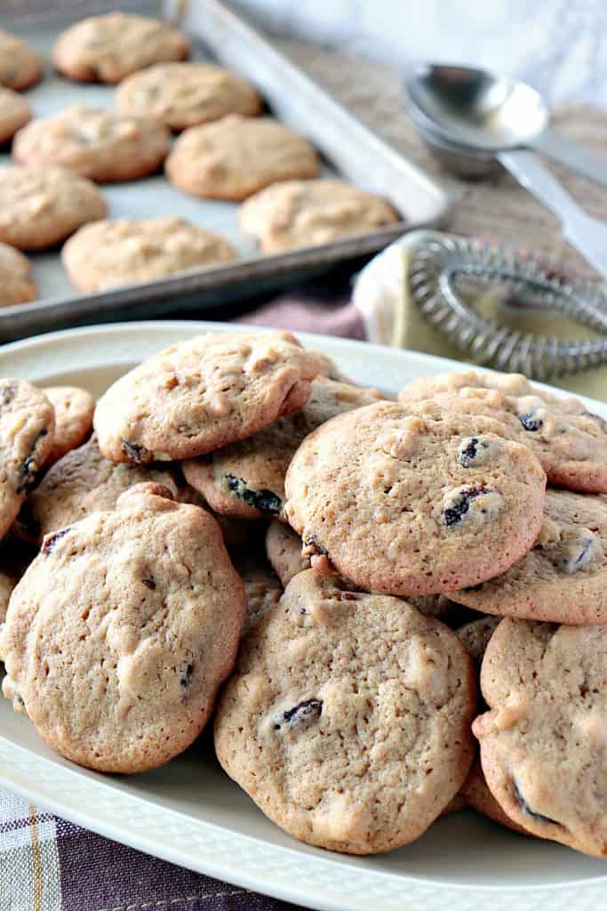 Vertical photo of a closeup of rocks cookies on a platter with a baking sheet filled with cookies in the background.