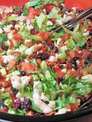 A colorful bowl filled with Winter Chopped Salad with cranberries, bacon, lettuce, and pecans.