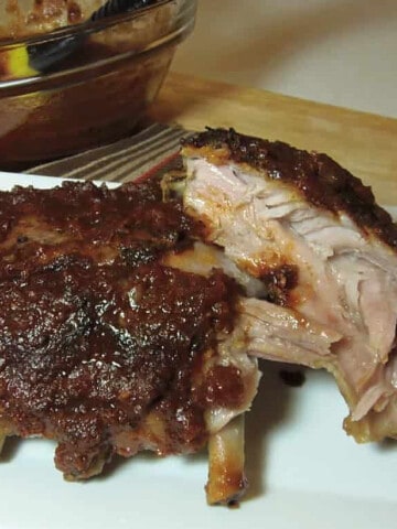 A rack of BBQ Salsa Baby Back Ribs with a bowl of BBQ sauce in the background.