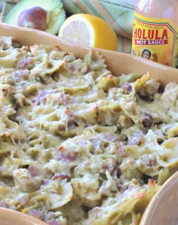 A casserole filled with a chicken artichoke pasta and an avocado and lemon in the background.