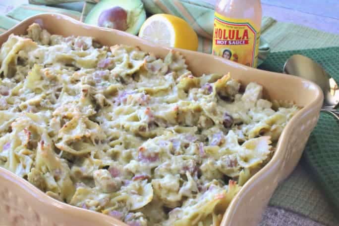 A casserole filled with a chicken artichoke pasta and an avocado and lemon in the background.