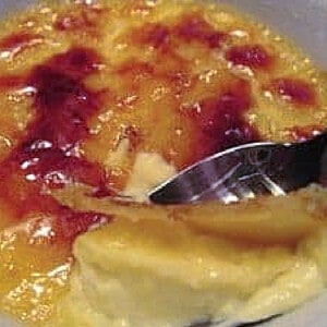 A spoon cracking into the sugar topping of an Orange Creme Brulee.