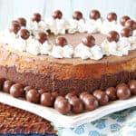 An entire Malted Milk Ball Cheesecake on a square white plate surrounded by malted milk balls.