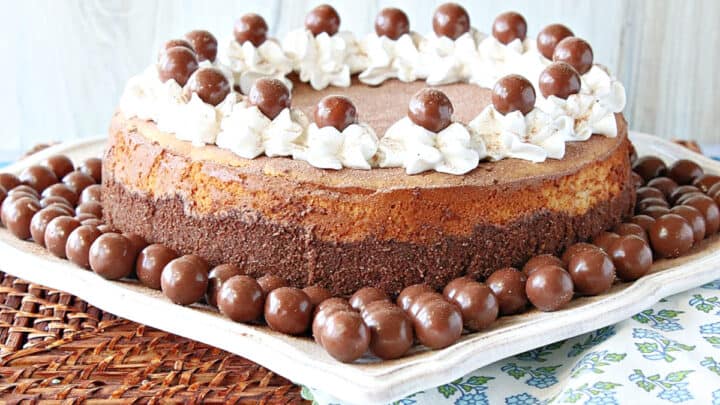 An entire Malted Milk Ball Cheesecake on a square white plate surrounded by malted milk balls.