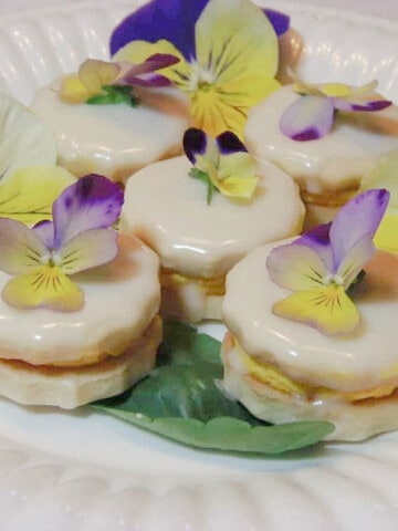A plate of pretty Lemon Custard Cream Cookies with pansies on top.