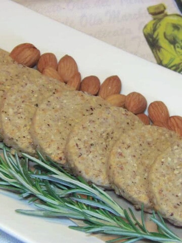 A row of Parmesan Sable crackers on a long plate with rosemary and almonds.