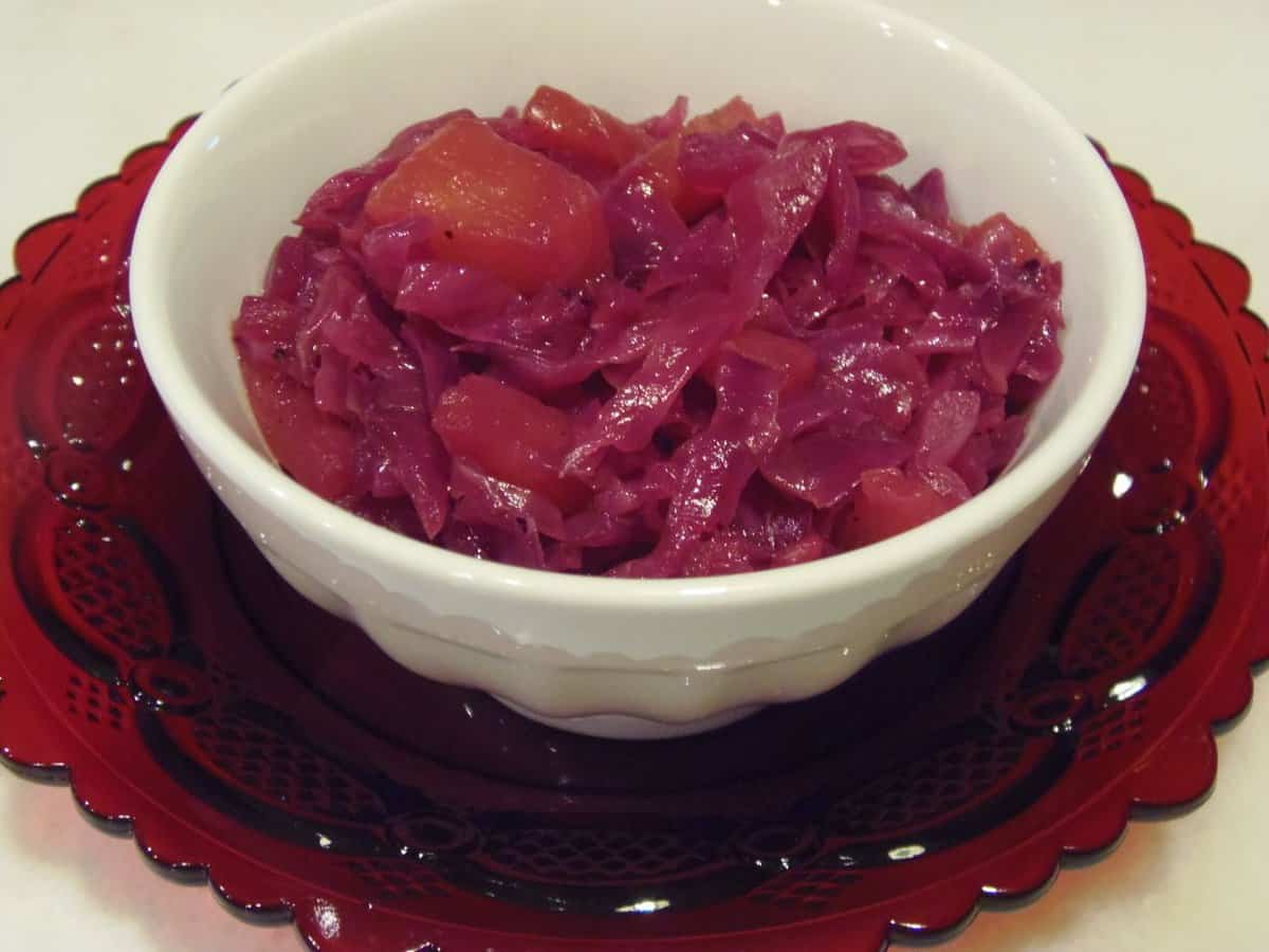 A small round white bowl filled with Sauteed Rid Cabbage with Pineapple on a red glass plate.
