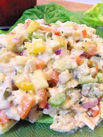 A colorful closeup of a serving of Rainbow Chicken Salad on a bed of lettuce leaves.