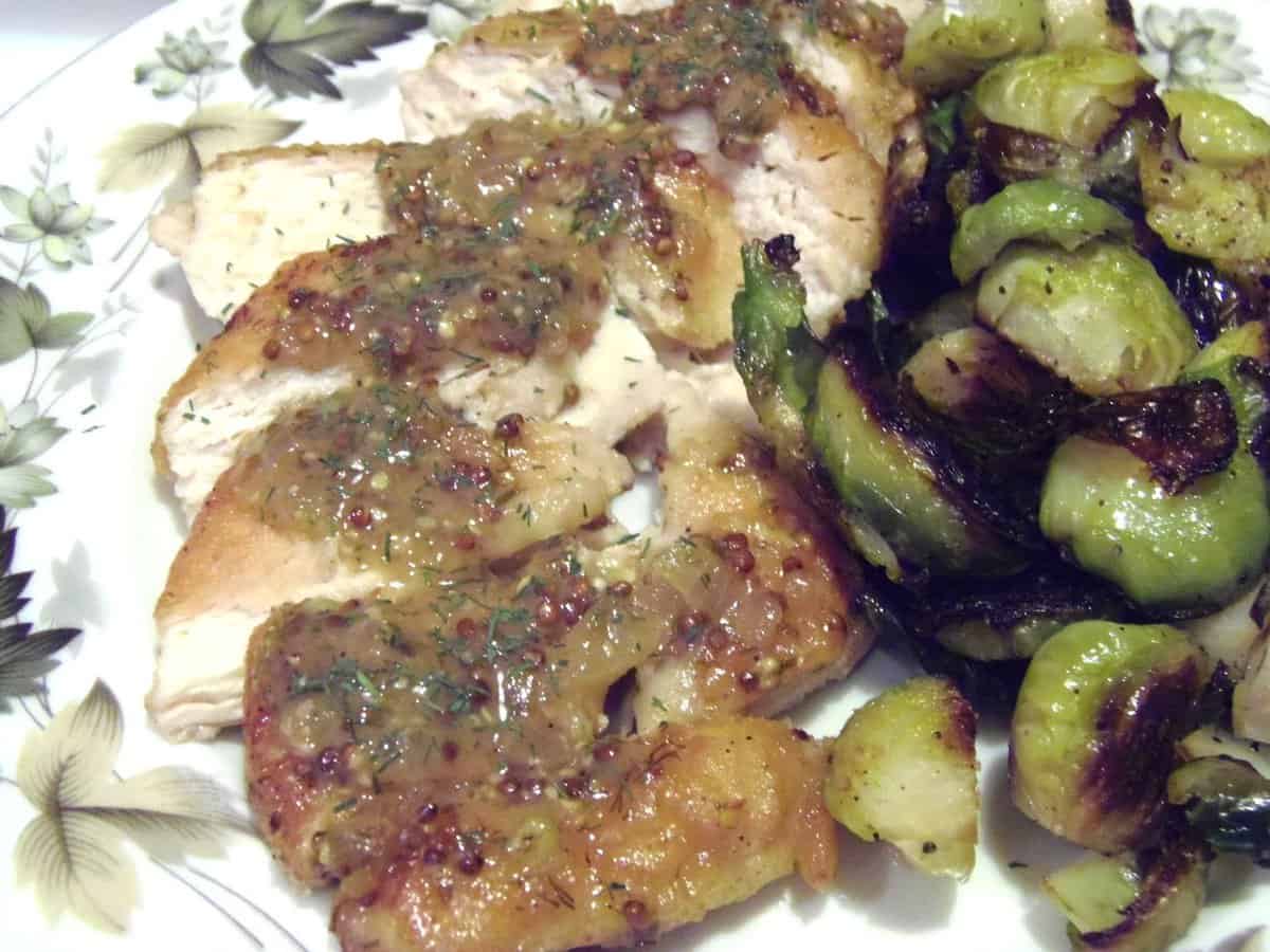 Sliced Chicken breast covered with mustard dill sauce on a plate with Brussels sprouts.