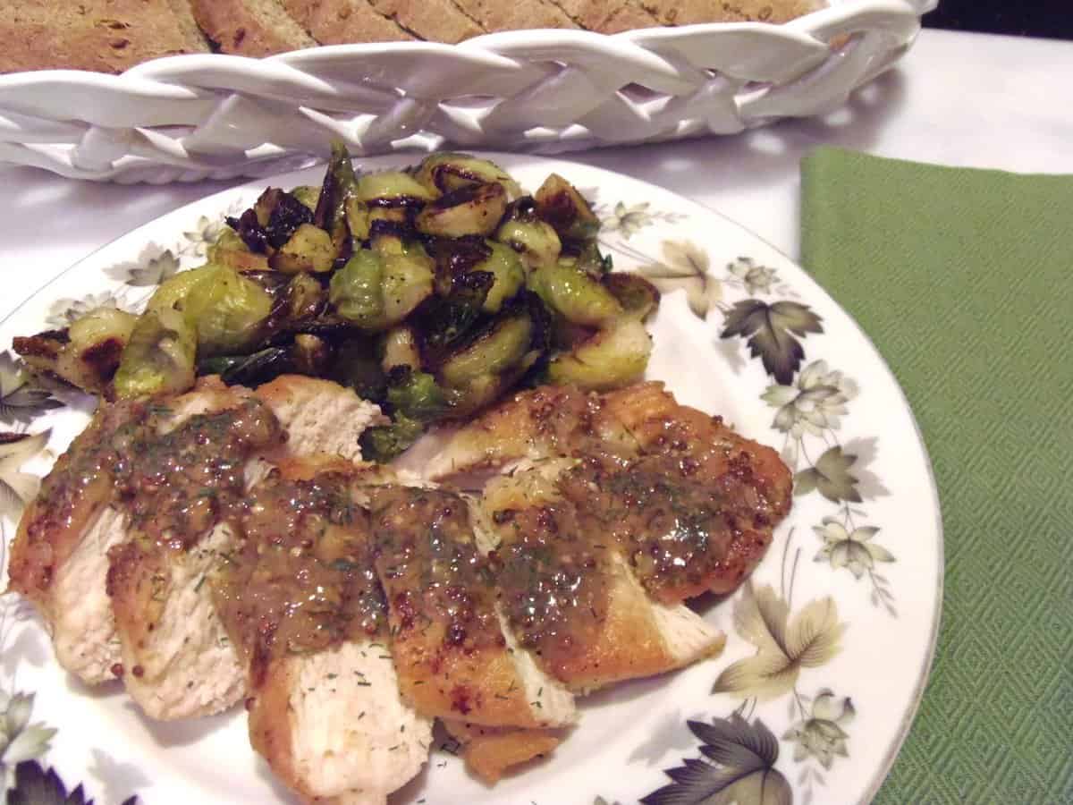 A serving plate with green leaves filled with sliced Chicken with Mustard Dill Sauce and Brussels sprouts.