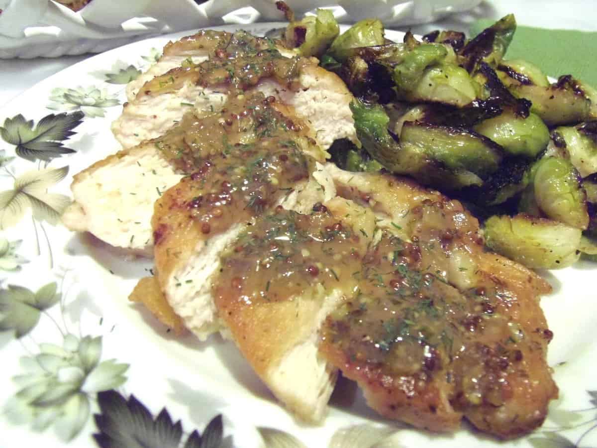 A sliced serving of Chicken with Mustard Dill Sauce on a plate with brussels sprouts.