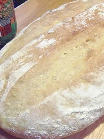 A floured loaf of No Knead Rustic Beer Bread on a wooden board.