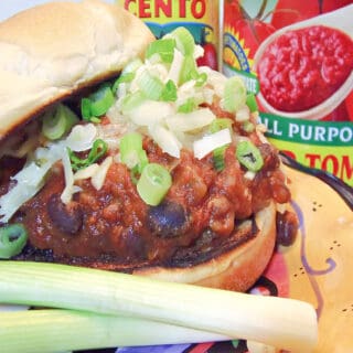 A closeup horizontal image of a Sloppy Jose Pork Sausage Sandwich with black beans and scallions.