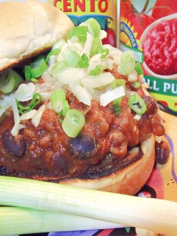 A closeup horizontal image of a Sloppy Jose Pork Sausage Sandwich with black beans and scallions.